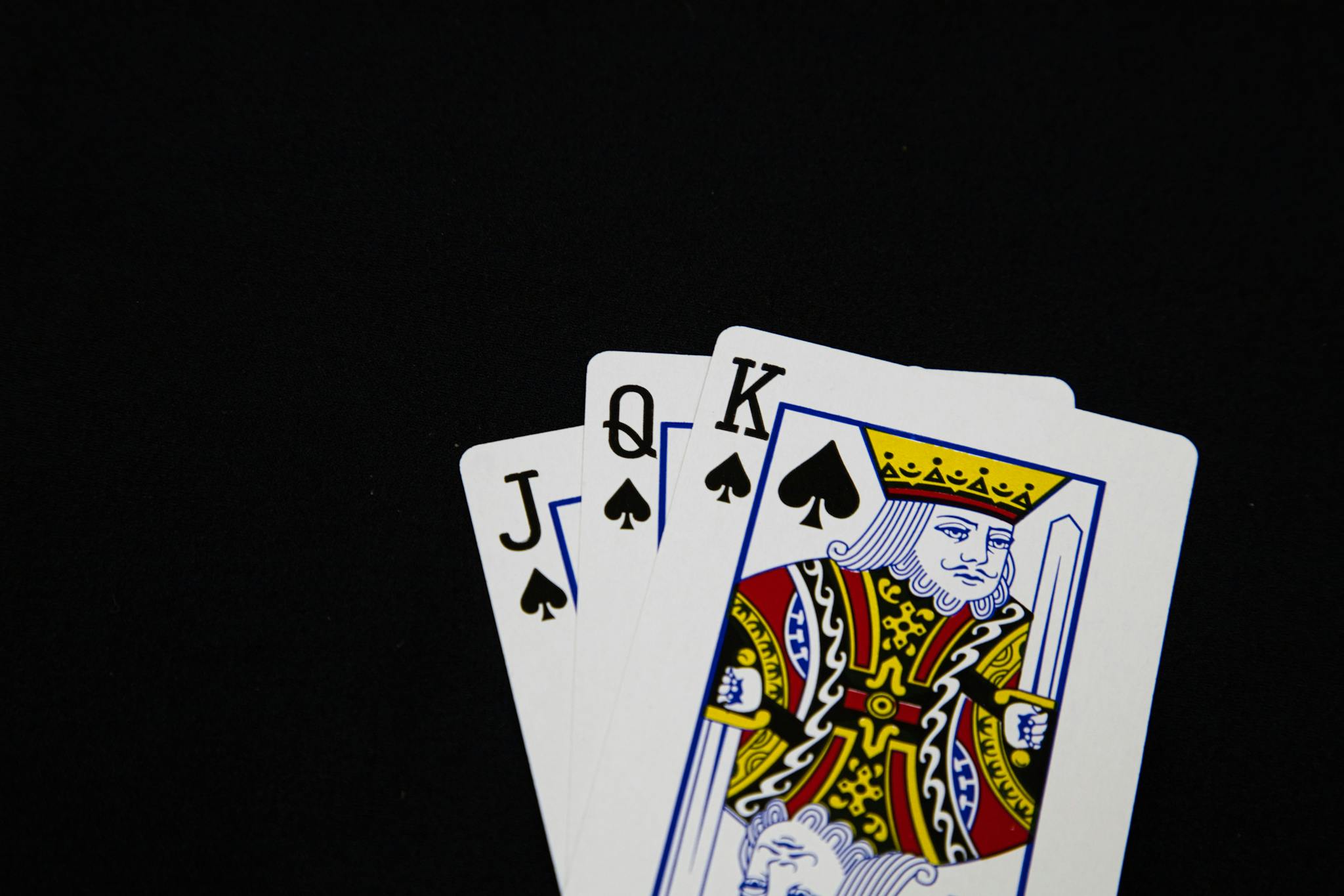 Close-up of Jack, Queen, King of Spades playing cards on black background.